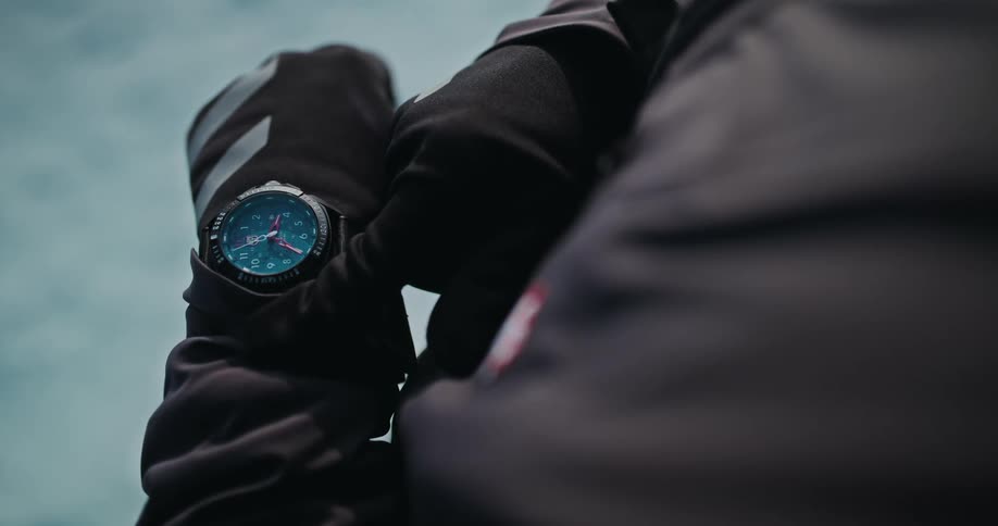 A close-up slow-motion shot of a person in black gloves checking their tactical smartwatch in an outdoor setting