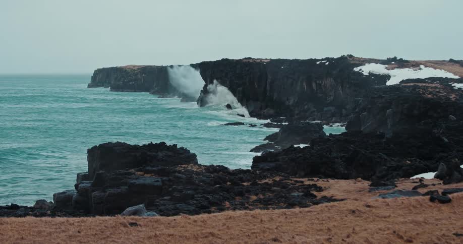Powerful turquoise ocean waves crash against the black volcanic cliffs of Iceland's coast in dramatic slow motion