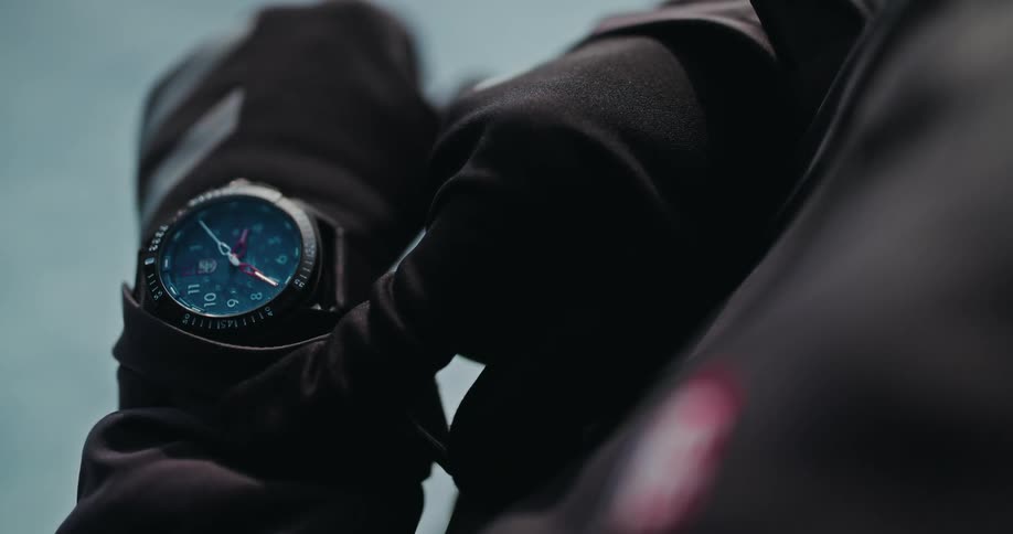 A person in black gloves and jacket reveals a smartwatch in a dramatic slow-motion close-up