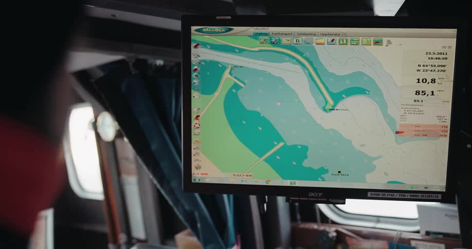 Over the shoulder shot of a sailor pointing at a digital navigation chart on a computer screen inside a boat's cabin