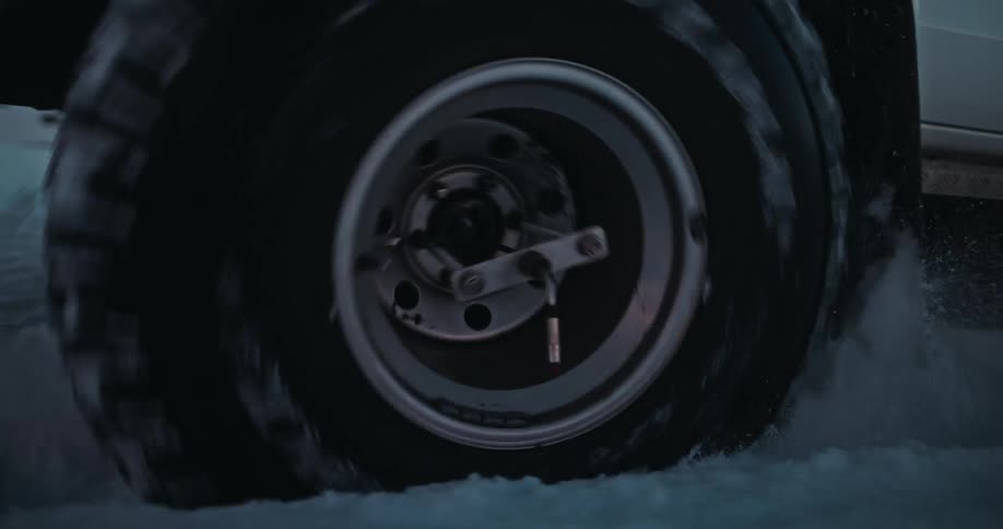 A close-up slow-motion shot of a powerful off-road vehicle's tires gripping and churning through deep snow in a desolate arctic landscape