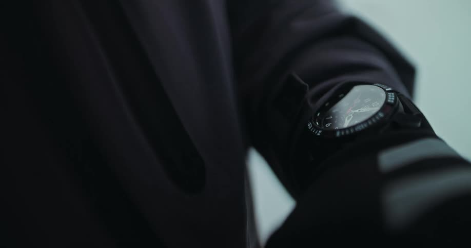 A cinematic slow-motion close-up of a person's athletic jacket, pulling focus to a modern sports watch on their wrist