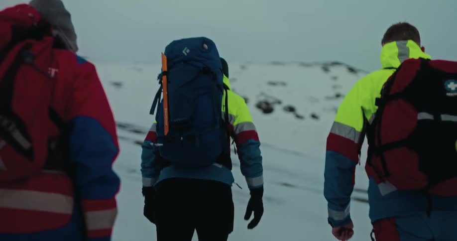 A search and rescue team equipped with backpacks and winter gear hikes up a snow-covered mountain slope on a mission