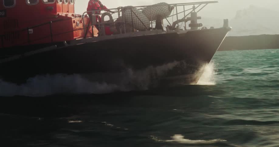 Slow motion of an Icelandic coast guard boat speeding through the choppy sea, with a crewman on deck and snowy mountains in the background