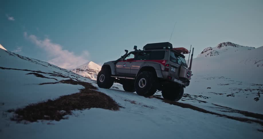 A rugged 4x4 expedition vehicle ascends a snowy mountain trail during a scenic adventure