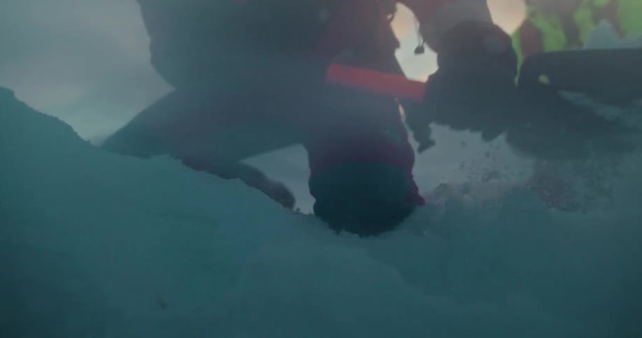A mountain rescue team urgently shovels deep snow in a dramatic slow-motion sequence during a training exercise