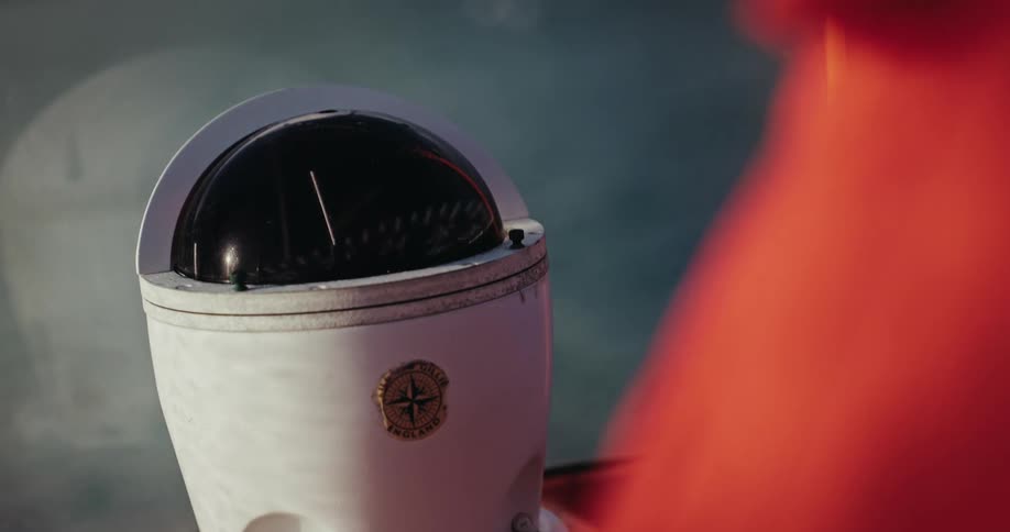 A classic gimbaled nautical compass on a moving boat sways gently with the motion of the water