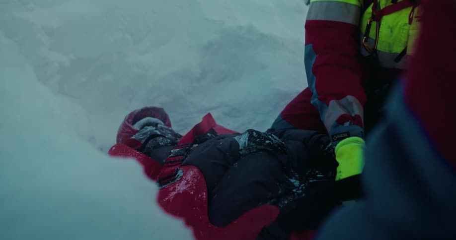 A mountain rescue paramedic carefully straps an injured person onto a stretcher in the deep snow