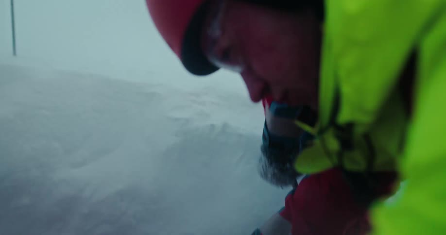 A mountain rescuer digs vigorously with a shovel to free a person buried in the snow during a winter storm