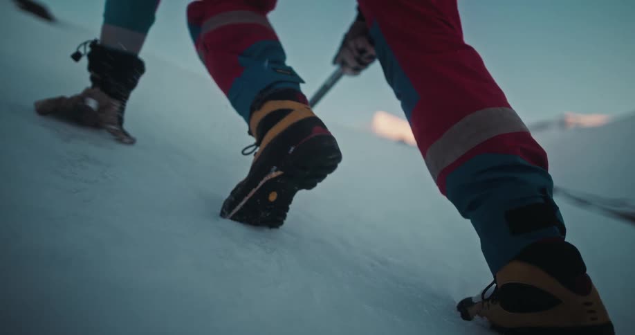 A mountain climber slowly ascends a steep snowy slope, digging an ice axe into the snow for grip