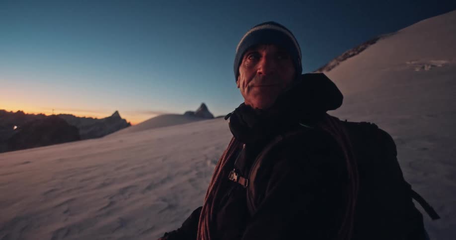 A seasoned alpinist pauses on a snowy ridge at dawn, with the majestic Matterhorn in the background