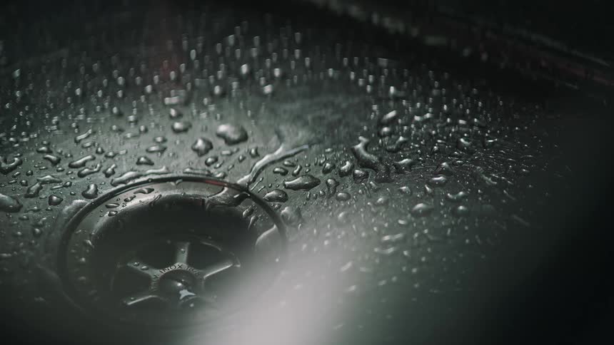 Moody slow-motion close-up of water dripping into a wet stainless steel sink near the drain