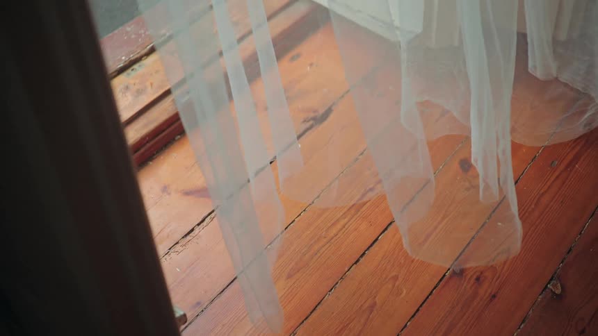 A sheer white curtain gently sways in the breeze above a rustic hardwood floor, illuminated by soft light
