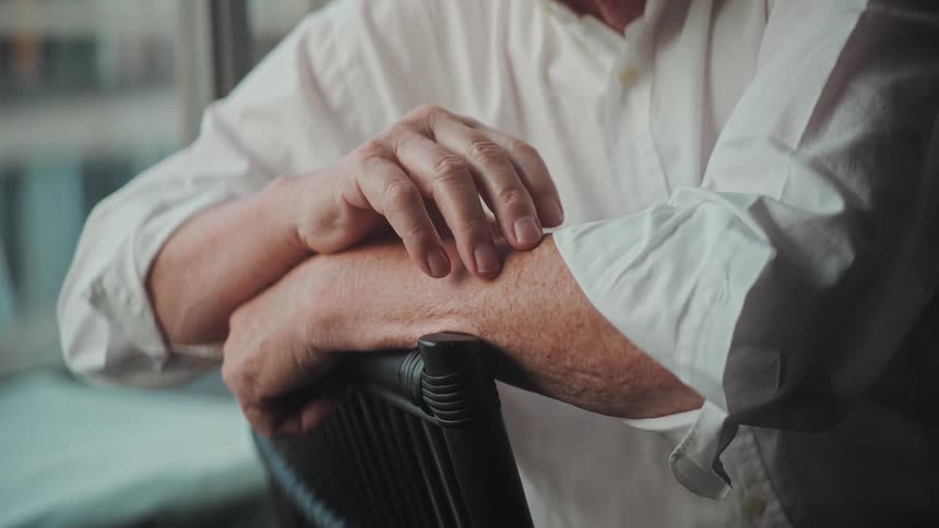 A close-up shot focuses on the weathered hands of an elderly person resting thoughtfully on a chair
