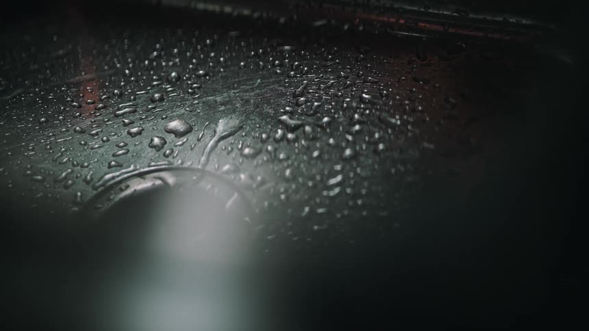 Dramatic slow motion shot of water droplets falling into a dark, wet stainless steel sink