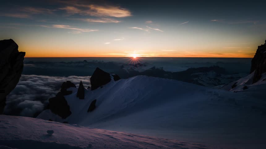 Stunning timelapse of the sun setting over a majestic, snow-covered mountain range above a sea of clouds