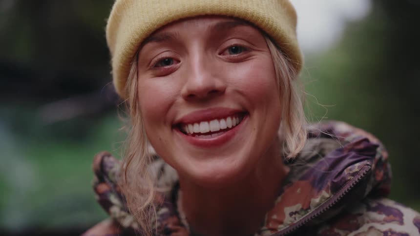 A cinemagraph portrait of a beautiful young woman with a joyful smile wearing a yellow beanie in a forest