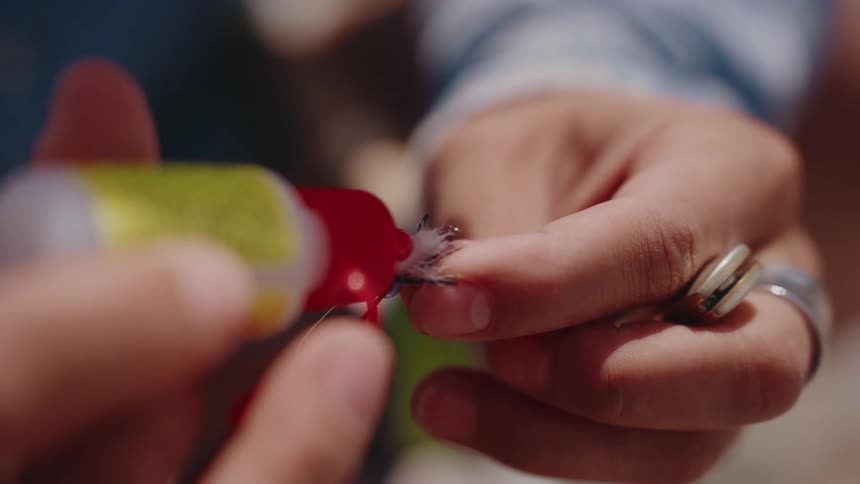 A fisherman meticulously applies floatant to a delicate fly fishing lure in a detailed close-up shot