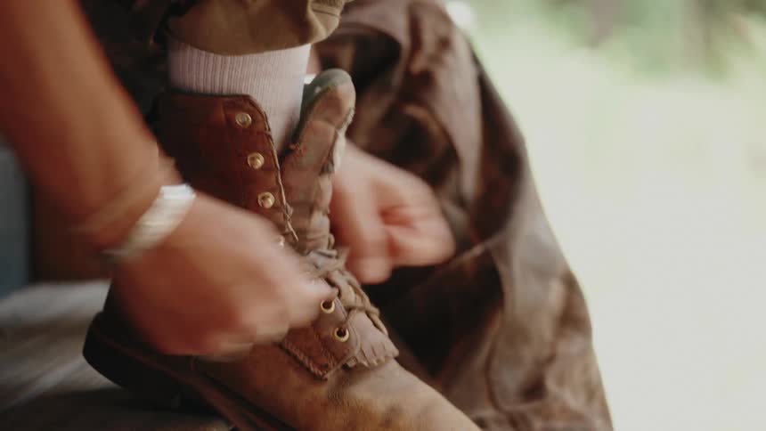 Close up of a person lacing up their rugged brown leather work boots while sitting on wooden steps