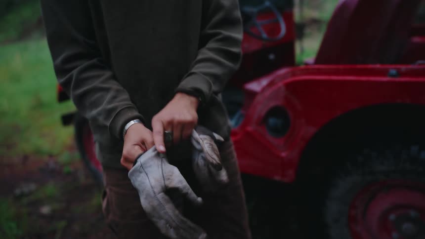 A woman wearing a yellow beanie gets out of her red off-road vehicle and puts on work gloves, preparing for work in the forest
