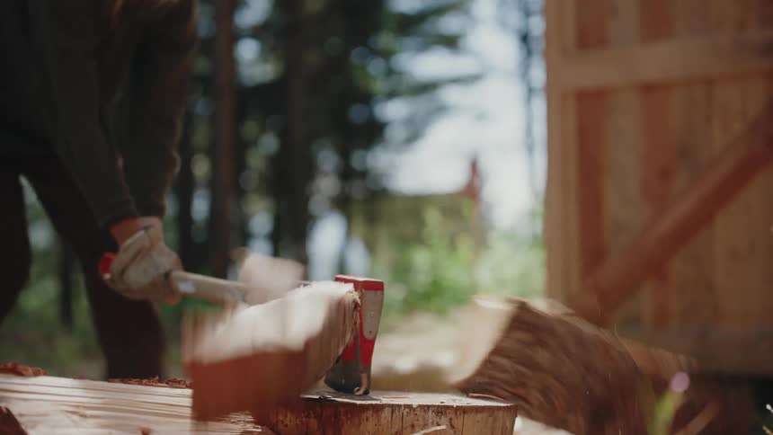 Close-up slow motion shot of a log being split in two by an axe in a forest setting