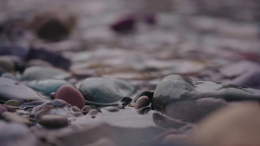 A serene close-up shot of a gentle stream flowing over colorful pebbles on a riverbed