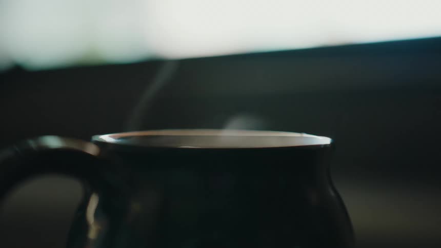 A close up cinematic shot of steam gently rising from a dark coffee mug in slow motion