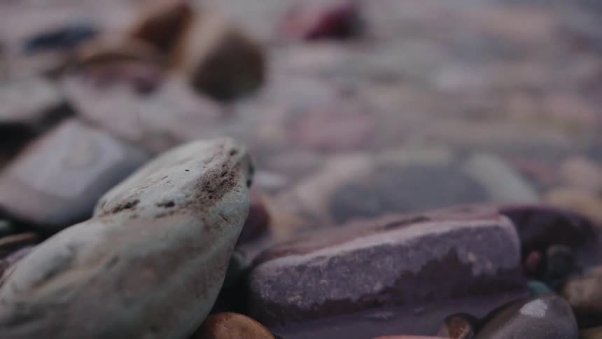 A peaceful macro shot of clear water gently flowing over colorful, smooth rocks in a shallow stream