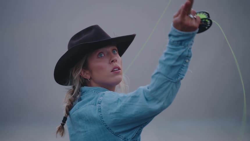 Slow motion shot of a woman in a denim shirt and hat skillfully casting her fly fishing line