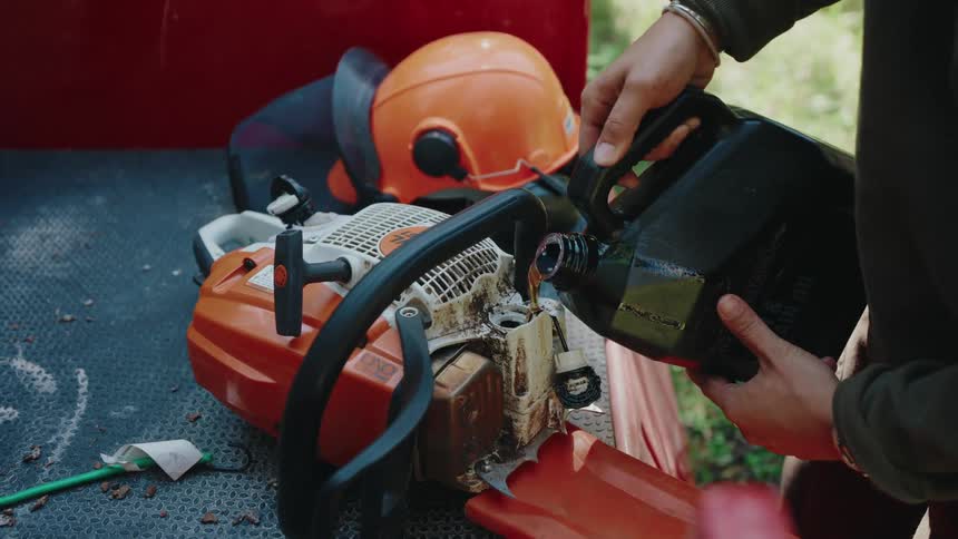 A worker performs routine maintenance by carefully pouring bar and chain oil into their chainsaw