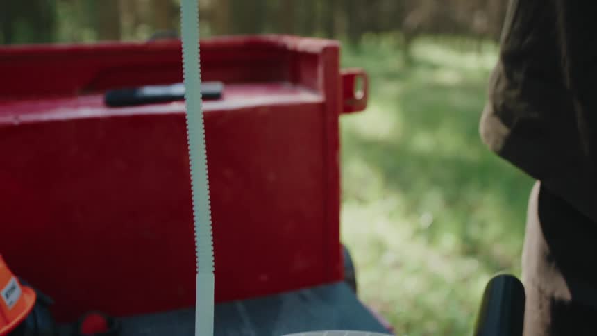 A woman wearing a beanie carefully pours fuel from a red gas can into a chainsaw in the forest