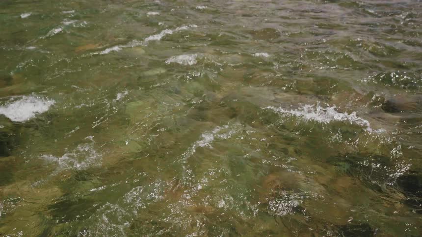 Gentle currents of a clear river ripple in slow motion over submerged rocks