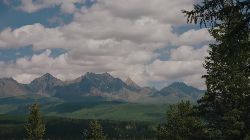 A scenic time-lapse captures clouds and their shadows moving across a vast mountain range and lush green forest