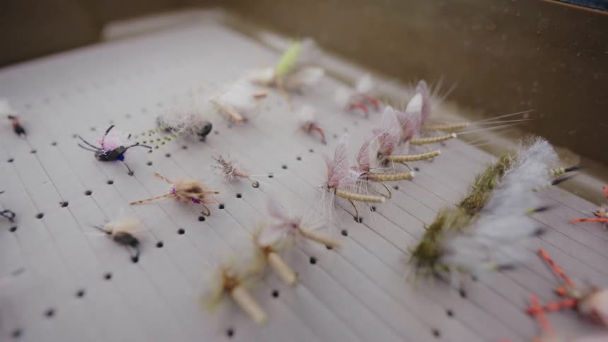 A close-up slow-motion reveal of an assortment of colorful, handmade fly fishing lures in a tackle box