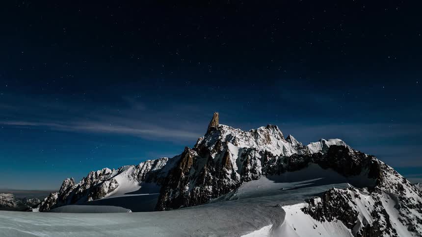 A stunning time-lapse of stars moving across the night sky over the snow-covered Alps, illuminated by bright moonlight