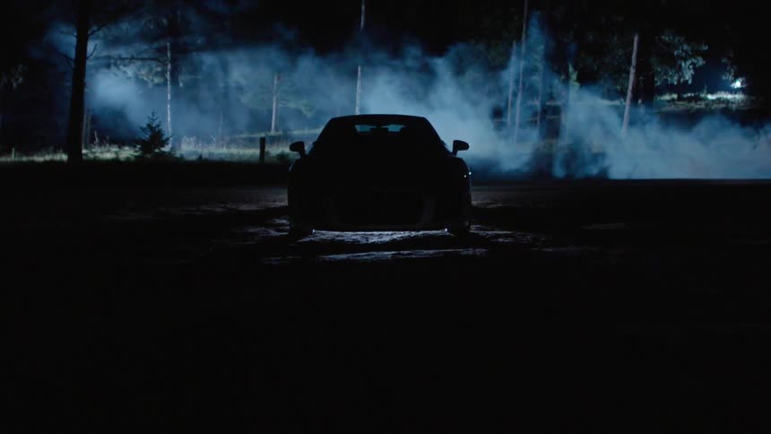 A car turns on its lights as fog stream into trees behind it
