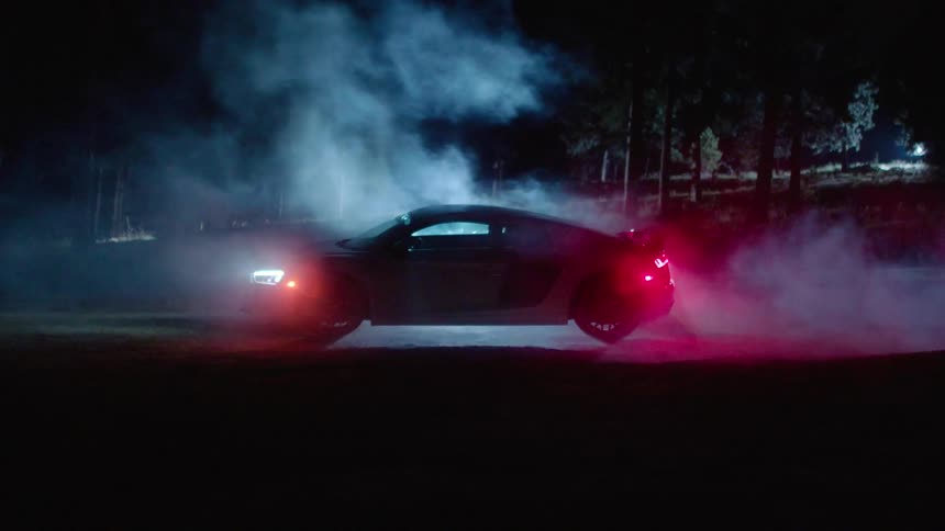 A car has fog rolling over it at night