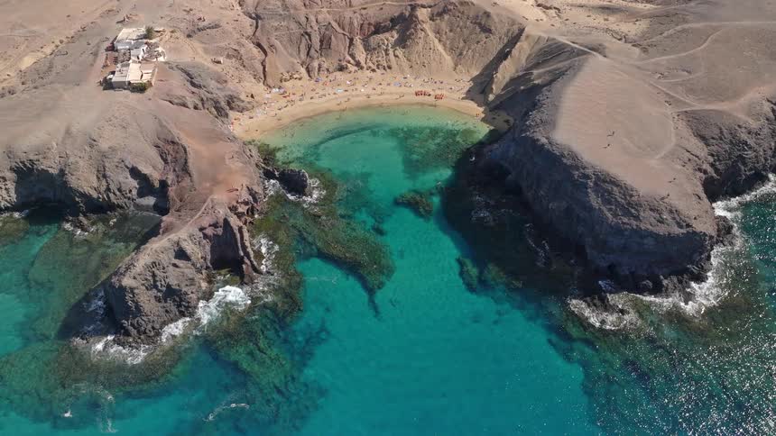 A breathtaking stationary aerial view of a beautiful volcanic cove with crystal-clear turquoise water and a golden sand beach