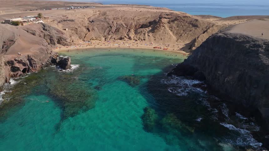 An aerial view pulls back from a beautiful turquoise bay to reveal a secluded sandy beach surrounded by dramatic cliffs