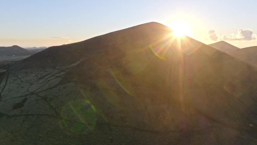 Stunning aerial shot of the sun rising from behind the peak of a dark, barren mountain, creating a beautiful lens flare