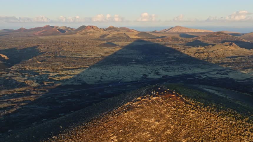 A stunning aerial view from a volcanic peak reveals its long, triangular shadow cast over a vast, arid landscape at sunrise