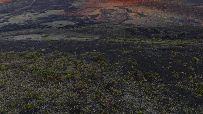 Aerial reveal of a stunning volcanic landscape with red craters glowing in the light of a beautiful sunrise