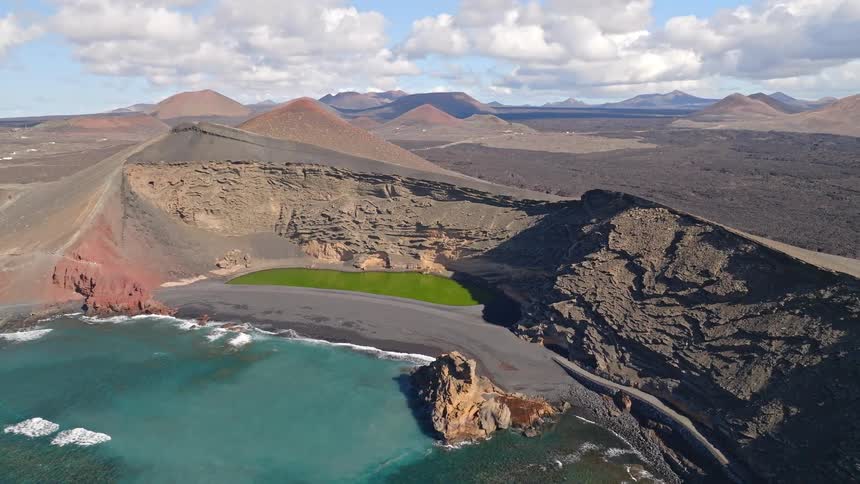 A stunning wide aerial view of the vibrant green lagoon, Charco de los Clicos, nestled in a volcanic crater on a black sand beach in Lanzarote