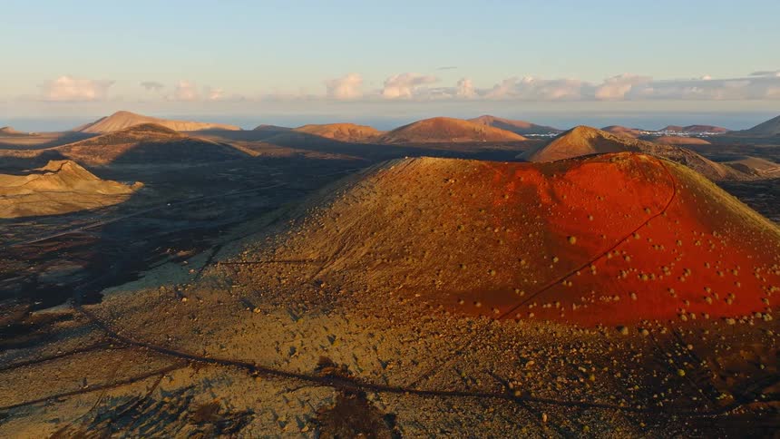 An epic ascending aerial view reveals a stunning red volcanic crater and surrounding volcanic landscape at sunrise
