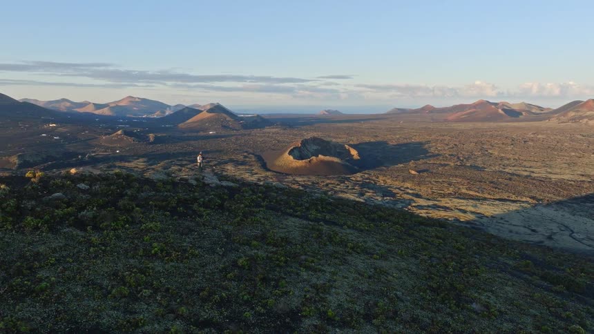 Epic aerial view of a couple standing on a volcanic peak at sunrise, with the mountain's perfect shadow cast over the vast crater-filled landscape below