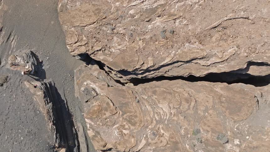 A top-down aerial view starts on a lone woman walking through a deep, narrow canyon and pulls up to reveal the immense scale of the rocky, volcanic landscape