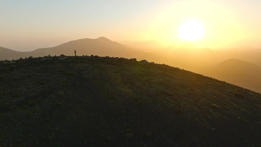 A lone runner is silhouetted against the golden sunrise while jogging along the crest of a mountain