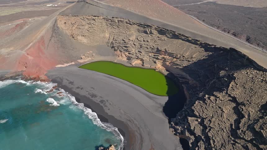 Cinematic aerial pullback reveals the famous green lake El Golfo within a volcanic crater on the dramatic coastline of Lanzarote, Canary Islands