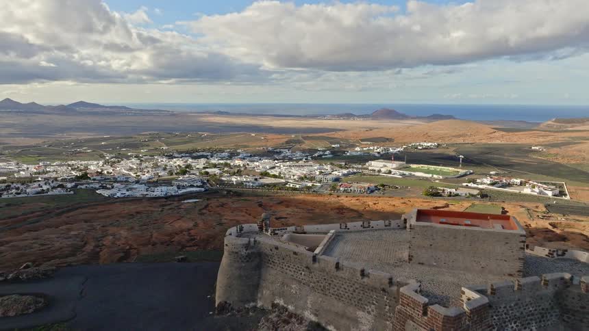A sweeping aerial view reveals the historic Castillo de Santa Barbara overlooking the town of Teguise and the vast landscape of Lanzarote