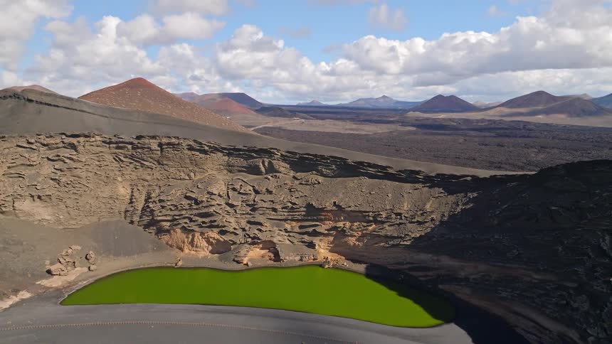 Dramatic aerial footage reveals the unique landscape of Lanzarote, featuring the vibrant green lagoon, a black sand beach, and the surrounding volcanic terrain